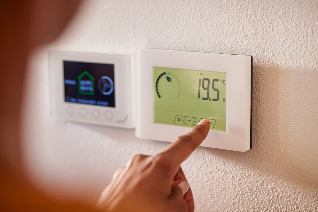 Woman adjusting a wall-mounted thermostat to increase heating temperature in a home.